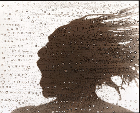 Silhouette of a man's head with dreads blowing behind him face a spray of water drops