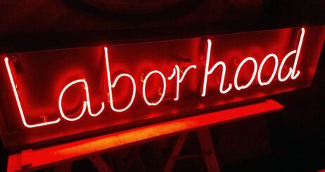 The image is of a neon sign that reads "Laborhood" in red against a dark background.